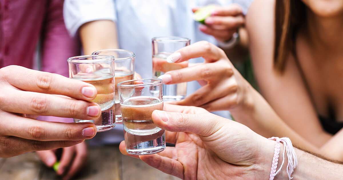close up of friends toast with tequila shots